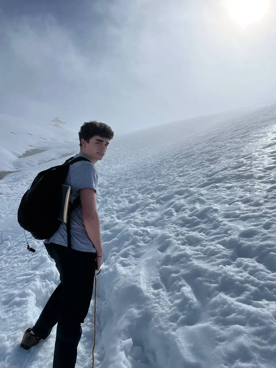 Friend with a backpack climbing through deep snow in the fog