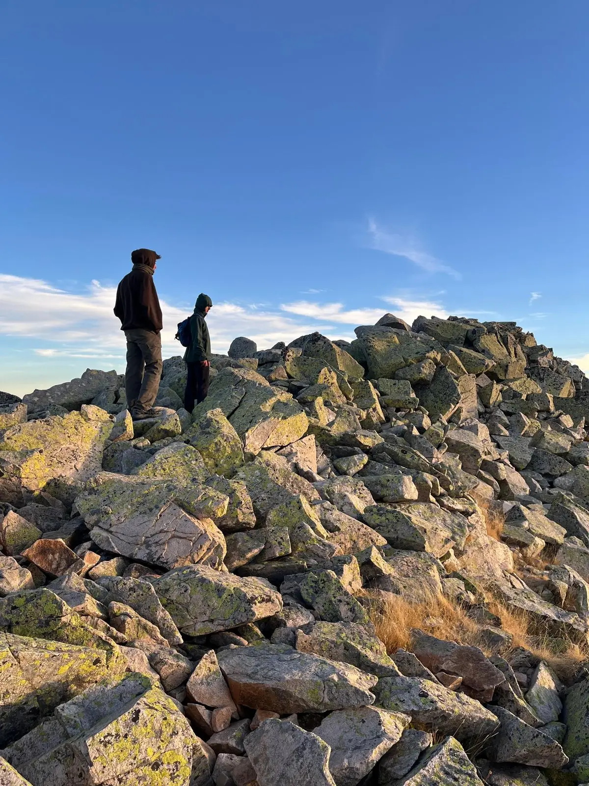 Two friends standing on a rocky summit at sunrise