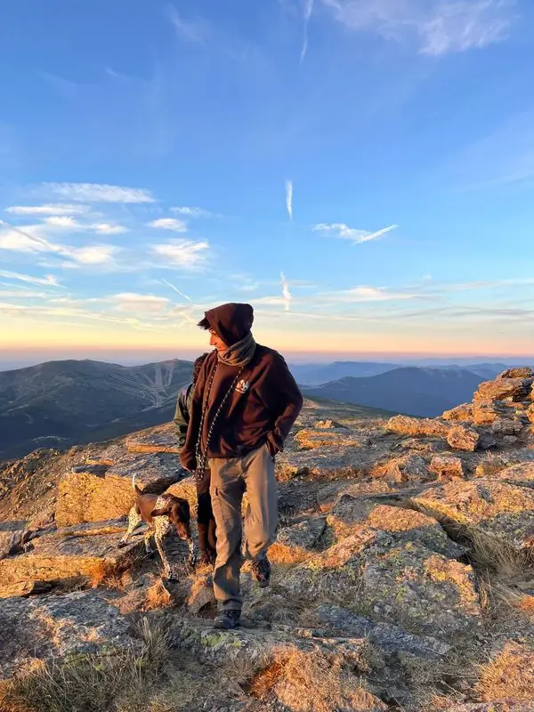 Hooded hiker with a dog on rocks at sunrise
